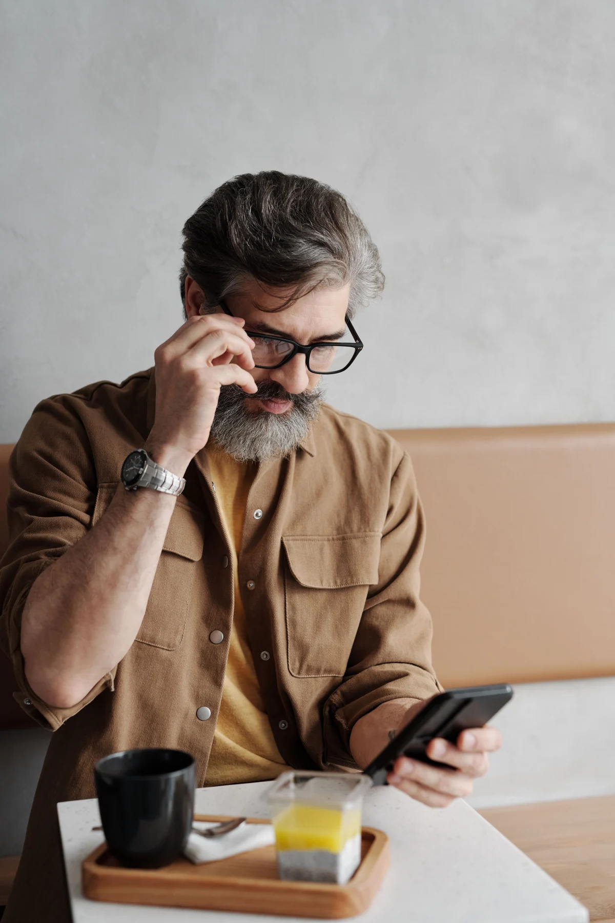 A bearded man in a brown overshirt reading beside his coffee